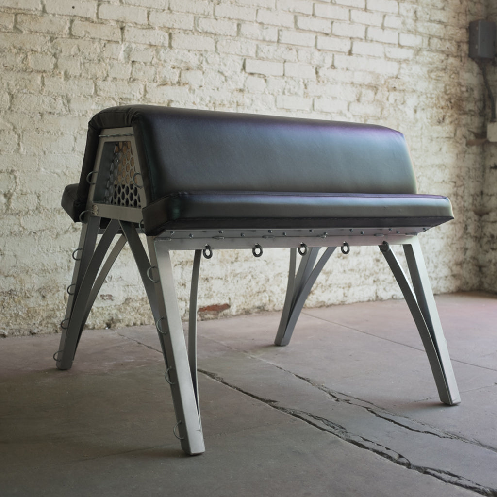 Stockroom Padded Spanking Bench — black vinyl over polished steel frame, perforated end plates, multiple rated attachment points along the body-rest edges.